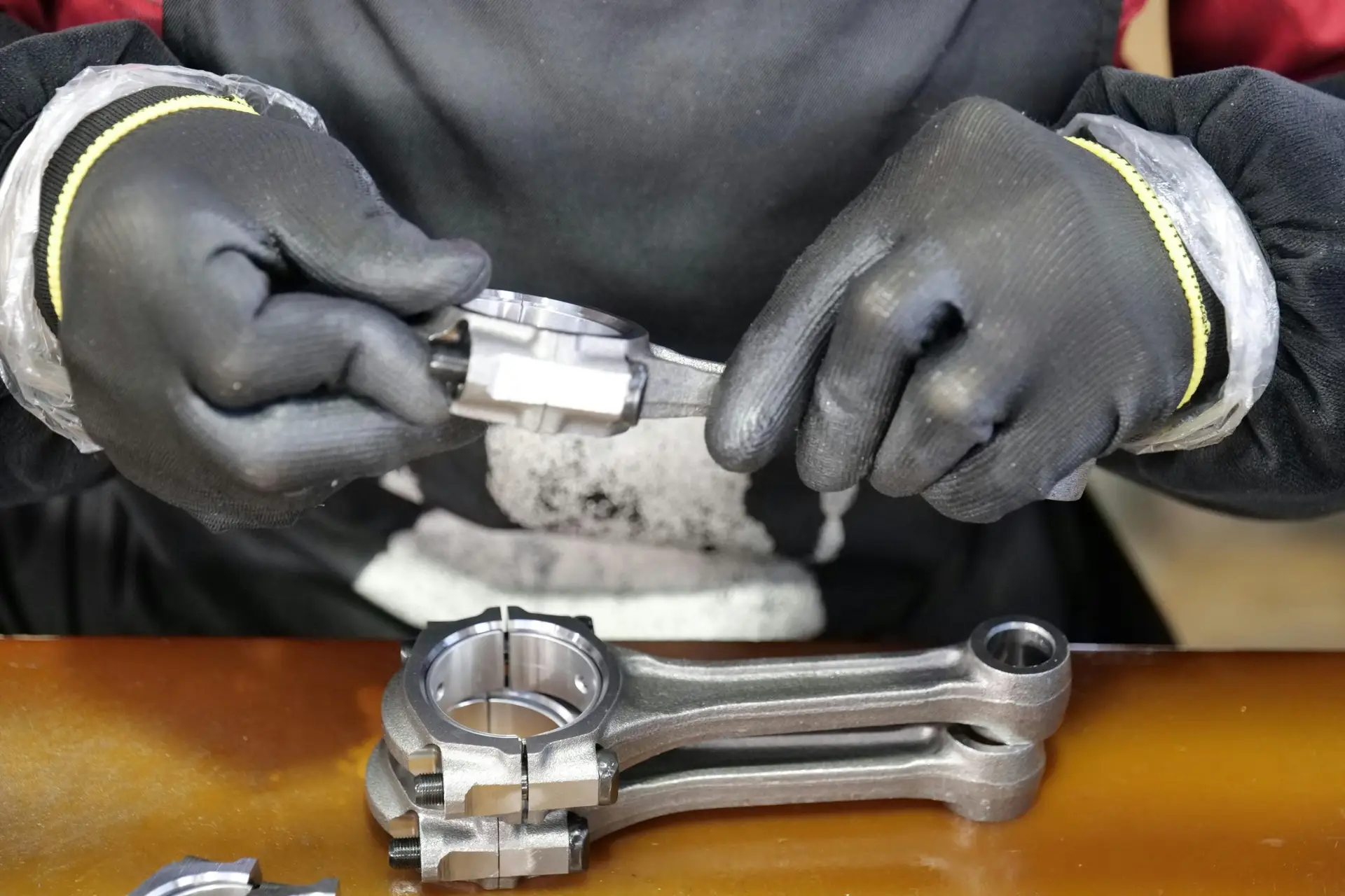 Close-up of a technician's hands assembling a metal connecting rod with precision and care.